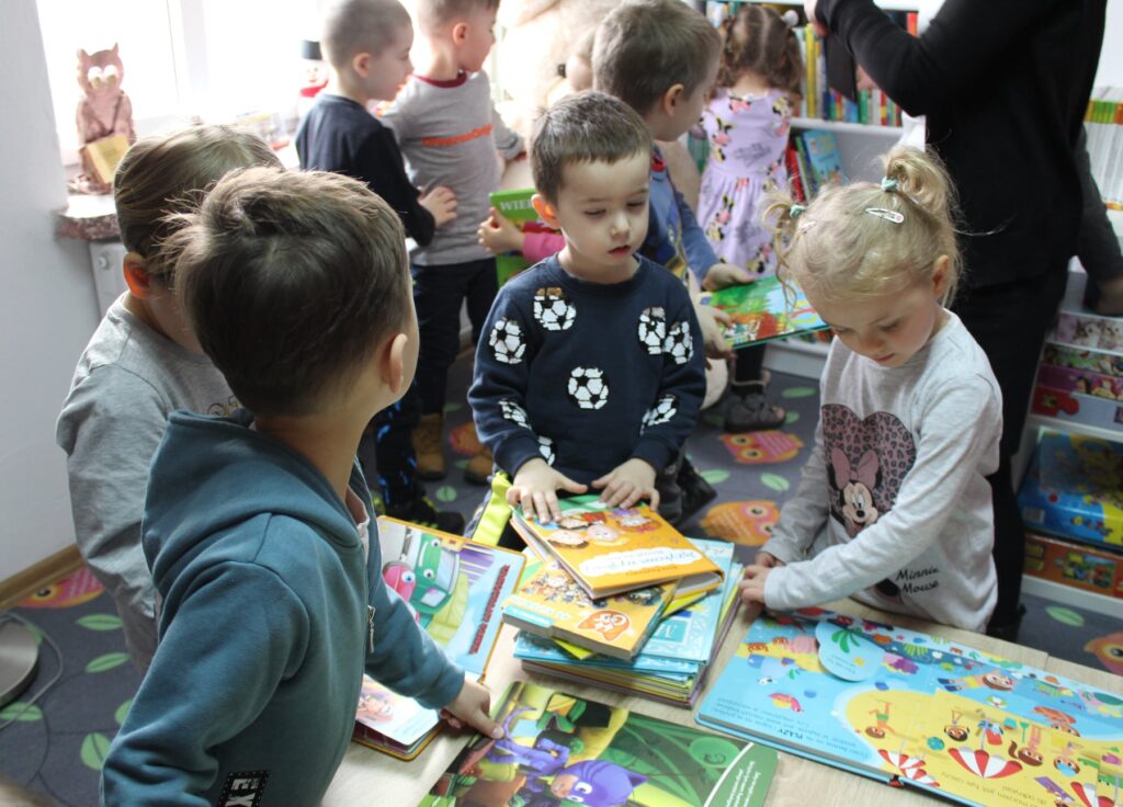 Grupa dzieci z wielkim zainteresowaniem ogląda kolorowe książeczki.