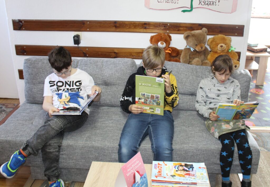 Kilkoro dzieci z wielkim zainteresowaniem oddaje się lekturze.
