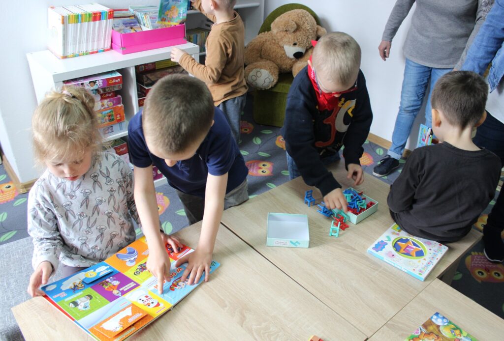 Na zdjęciu grupa dzieci ogląda dziecięcy księgozbiór biblioteczny (książki i zabawki).
