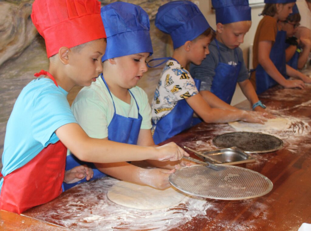 Zdjęcie przedstawia dzieci robiące pizze.
