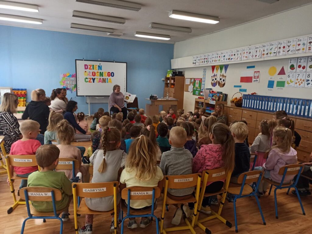 Zdjęcie przedstawia bibliotekarkę czytającą wiersze przedszkolakom.