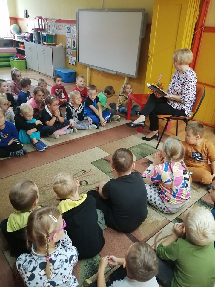 Zdjęcie przedstawia bibliotekarkę czytającą wiersze przedszkolakom.