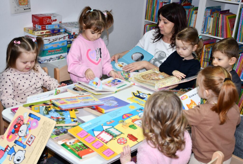 Na zdjęciu przedszkolaki z wychowawcą grupy podczas oglądania kolorowych książeczek.